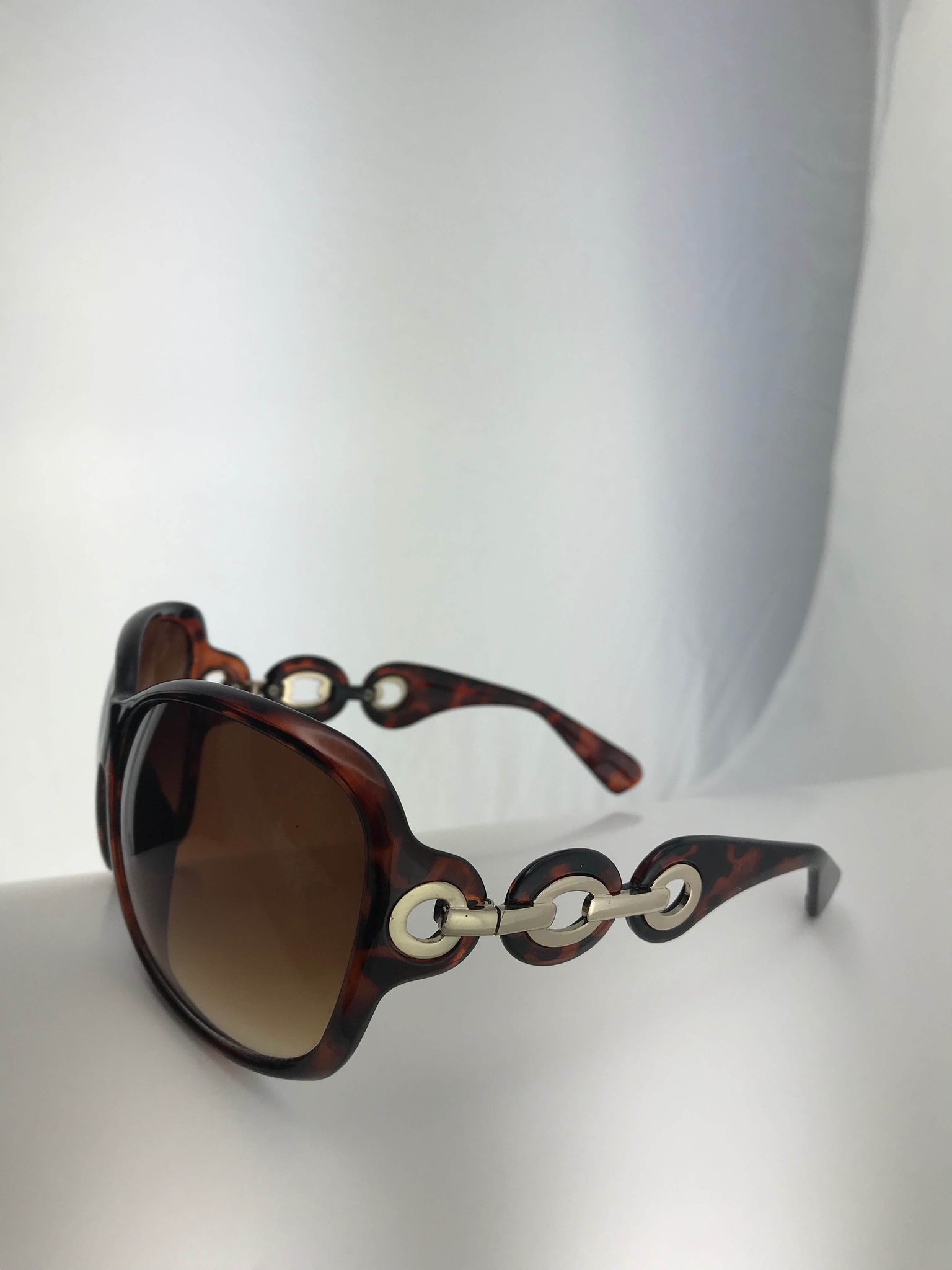 Oversized sunglasses with tortoiseshell or white frames, gold or silver links, and UV protection. Perfect for casual or formal looks.