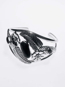 Handcrafted sterling silver cuff bracelet with intricate floral and feather motifs, adorned with polished black onyx stones