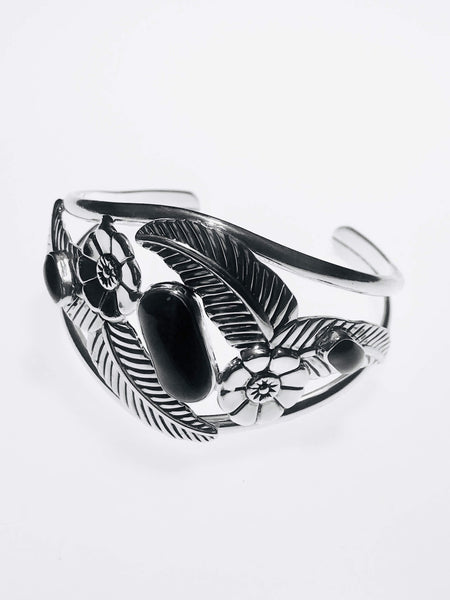 Handcrafted sterling silver cuff bracelet with intricate floral and feather motifs, adorned with polished black onyx stones