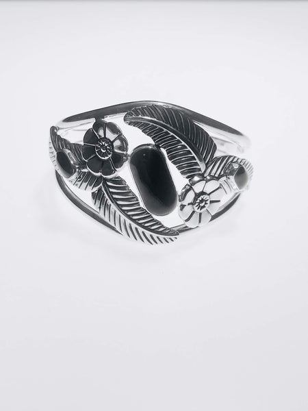 Handcrafted sterling silver cuff bracelet with intricate floral and feather motifs, adorned with polished black onyx stones